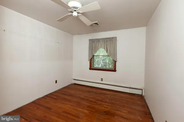 an empty room with wooden floor chandelier fan and windows