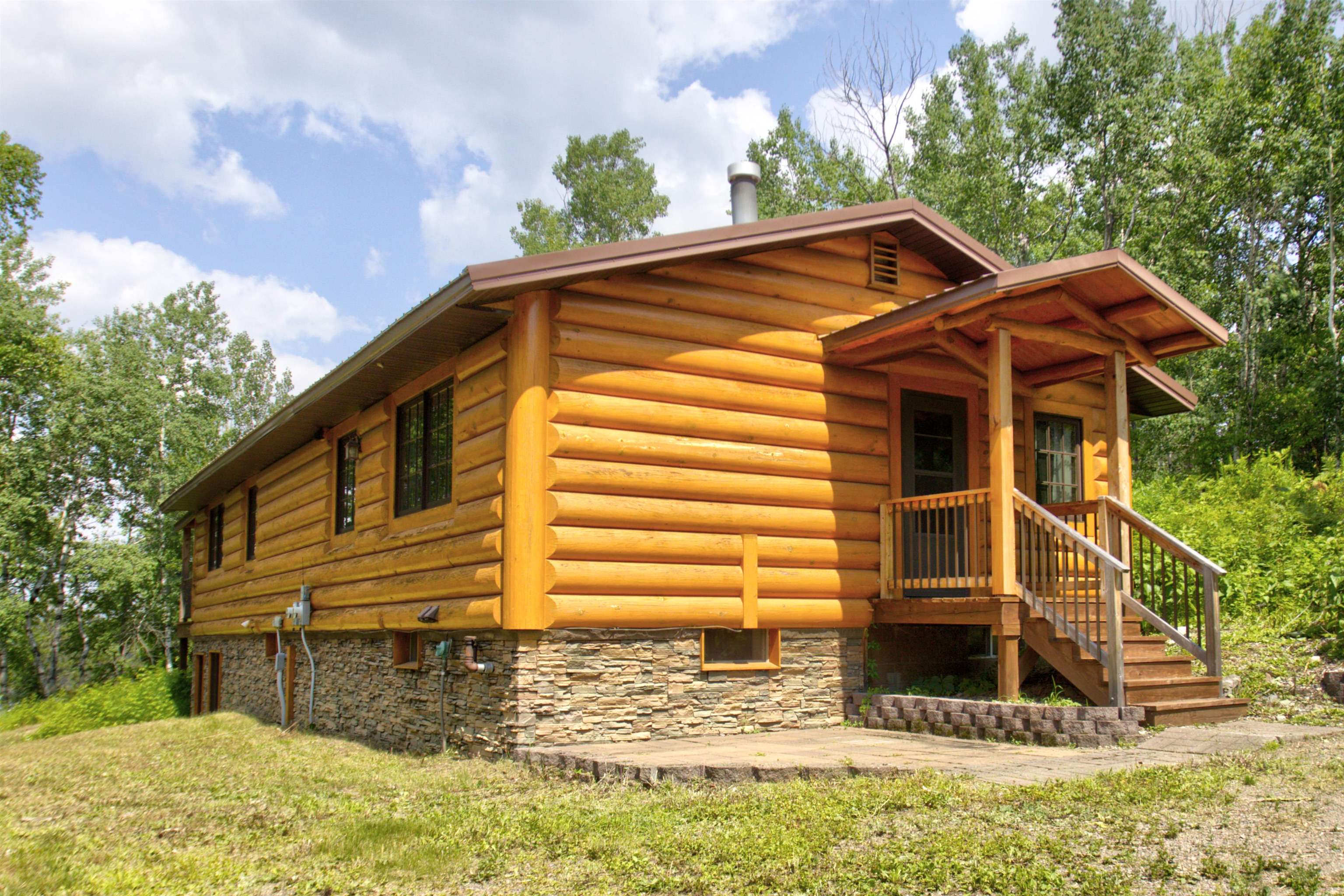 View of side of home with a porch, stone siding, and a yard