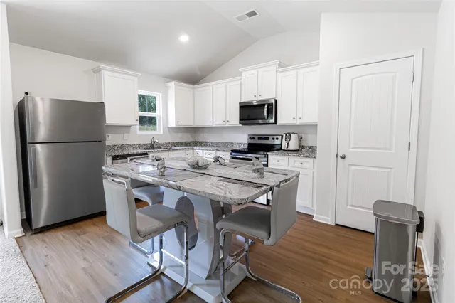 a kitchen with stainless steel appliances a refrigerator a stove a sink dishwasher and white cabinets with wooden floor