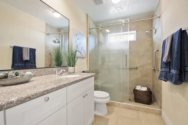a bathroom with a granite countertop sink a toilet a mirror a vanity and shower