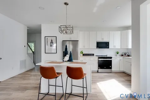 a kitchen with stainless steel appliances kitchen island granite countertop a stove top oven a sink a dining table and chairs with wooden floor