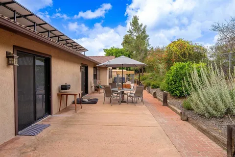 a view of a patio with table and chairs under an umbrella with large trees