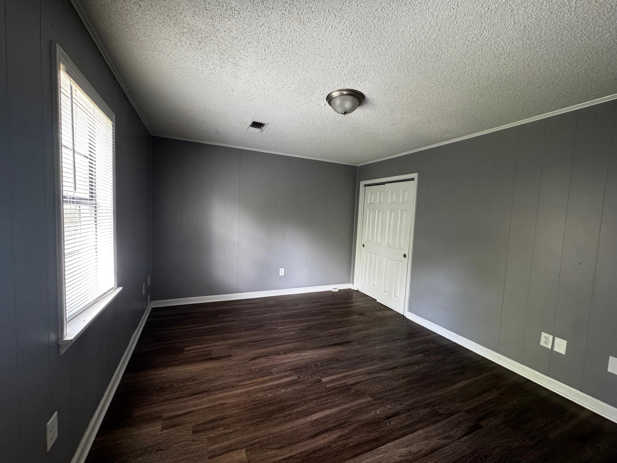 1112 Shoaf Road Covington, TN 38019 - Photo 11 of 17 Spare room featuring a textured ceiling, dark wood-style floors, crown molding, and wood walls