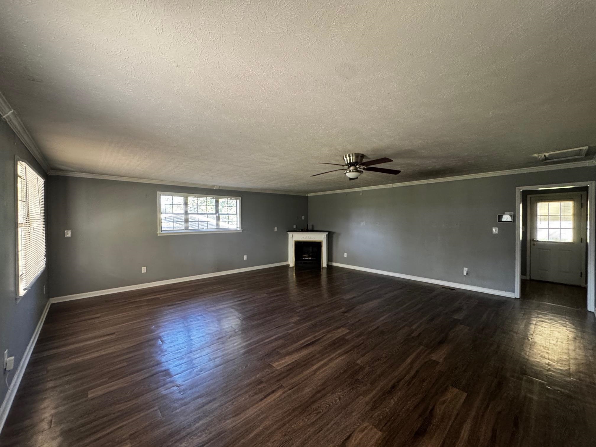 1112 Shoaf Road Covington, TN 38019 - Photo 4 of 17 Unfurnished living room with a ceiling fan, plenty of natural light, dark wood-type flooring, and crown molding