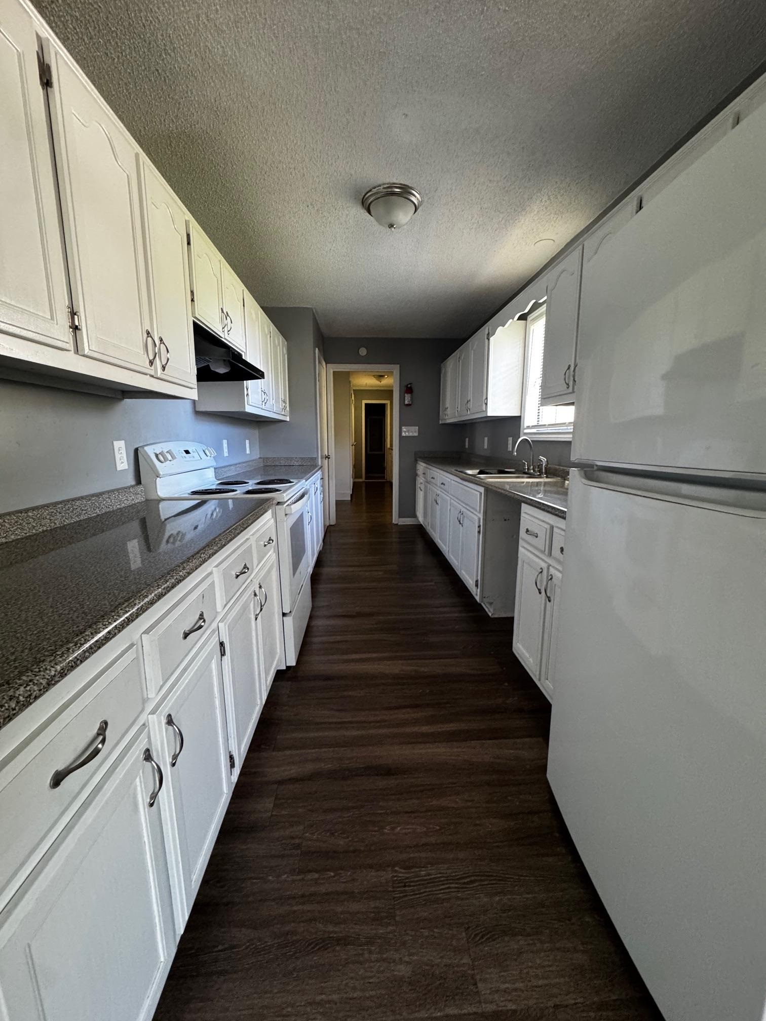 1112 Shoaf Road Covington, TN 38019 - Photo 8 of 17 Kitchen with white appliances, white cabinets, a textured ceiling, dark wood-style floors, and dark stone counters