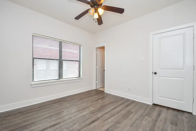 an empty room with wooden floor chandelier fan and windows