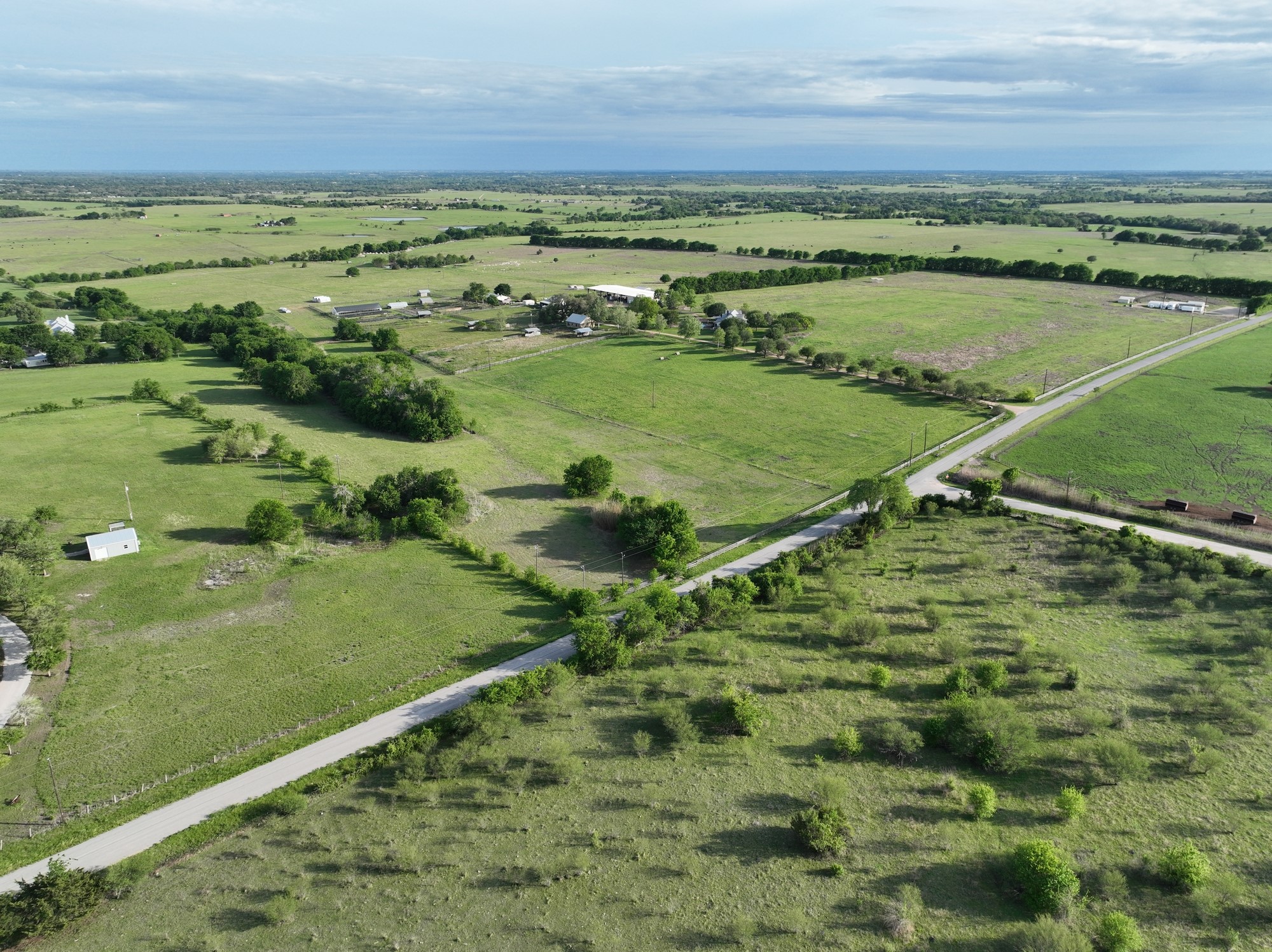 5255 Ganske Road Burton, TX 77835 - Photo 1 of 46 Expansive rural landscape with lush green fields and scattered trees. A winding road provides access through the spacious, open countryside. Ideal for those seeking tranquility and space.
