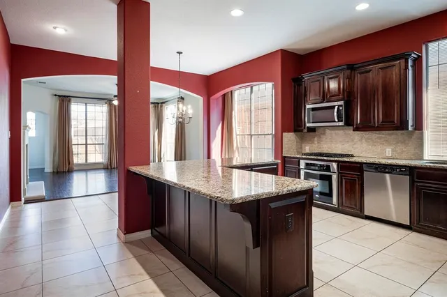 a kitchen with stainless steel appliances kitchen island granite countertop a refrigerator a stove and a sink with wooden cabinets