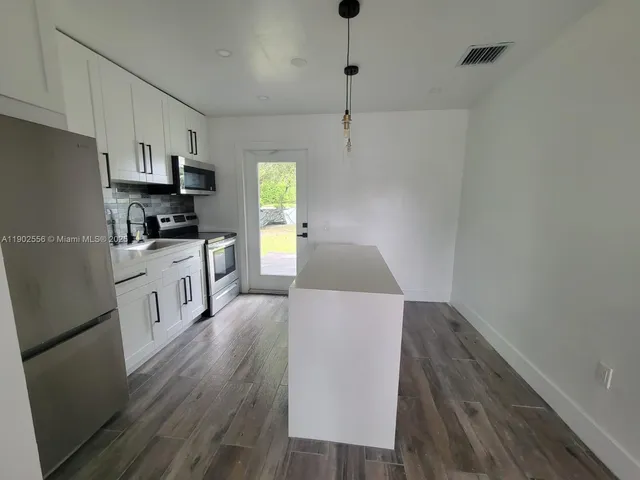 a kitchen with granite countertop a refrigerator a sink dishwasher a stove and white countertops with wooden floor