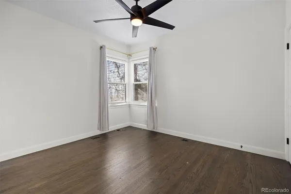 an empty room with wooden floor chandelier fan and windows