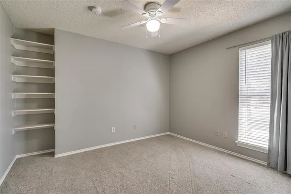 an empty room with a chandelier fan and windows