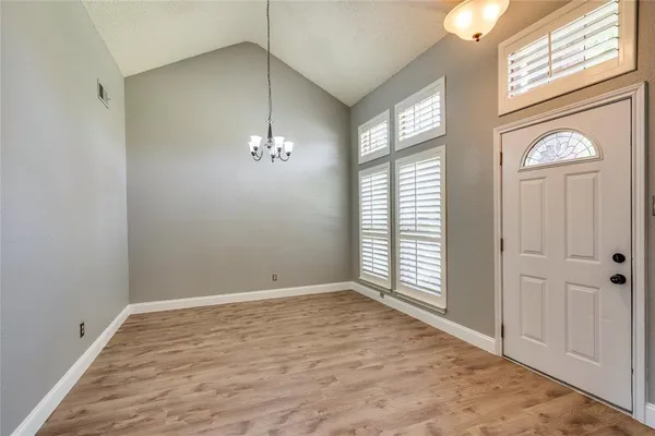 an empty room with wooden floor a chandelier fan and windows