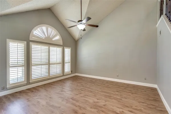 an empty room with wooden floor a ceiling fan a fireplace and windows