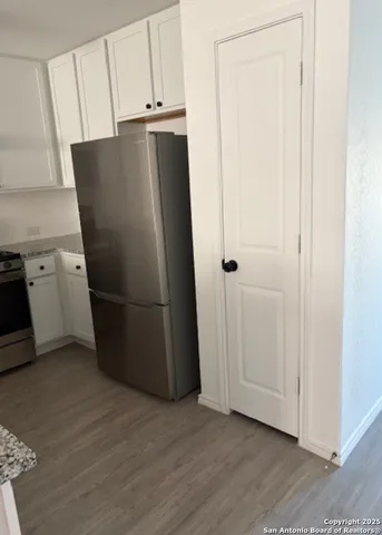 a view of a refrigerator in kitchen and empty room with wooden floor