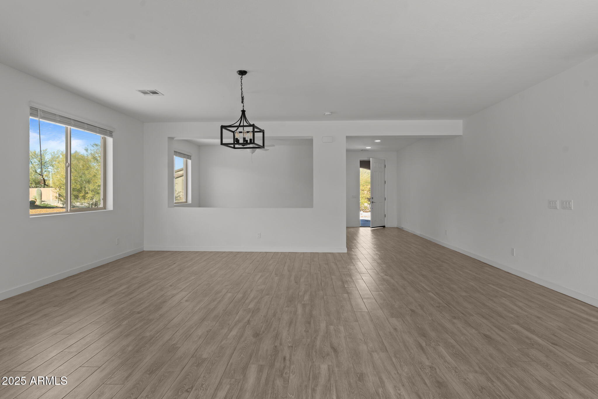 1985 West Ringo Road Wickenburg, AZ 85390 - Photo 9 of 25 an empty room with wooden floor chandelier and windows
