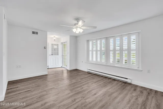 an empty room with wooden floor chandelier fan and windows