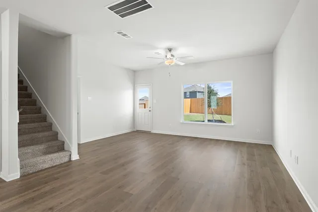 an empty room with wooden floor chandelier fan and windows
