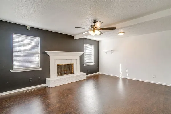 an empty room with wooden floor fireplace fan and windows