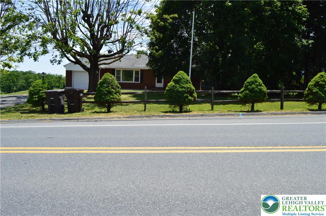 A classic brick-front home featuring a well-kept lawn and a charming split-rail fence.