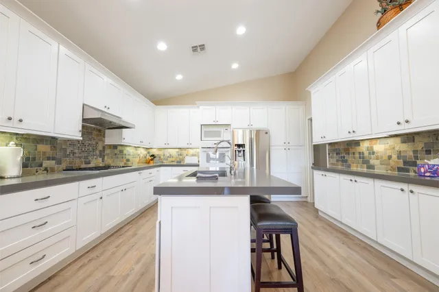 a kitchen with stainless steel appliances granite countertop a sink dishwasher a stove and white cabinets with wooden floor