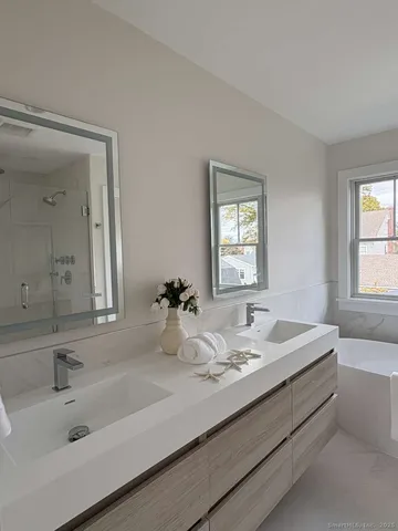 a bathroom with double vanity sinks with tub and mirror