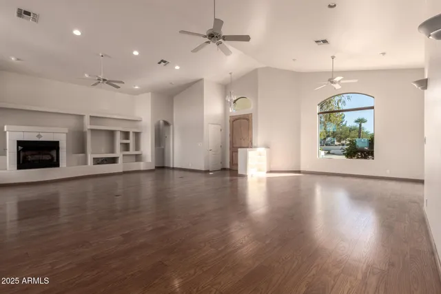 an empty room with wooden floor fireplace and windows