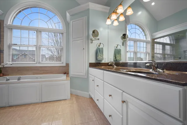 a spacious bathroom with a double vanity sink a two mirror a window and a bathtub