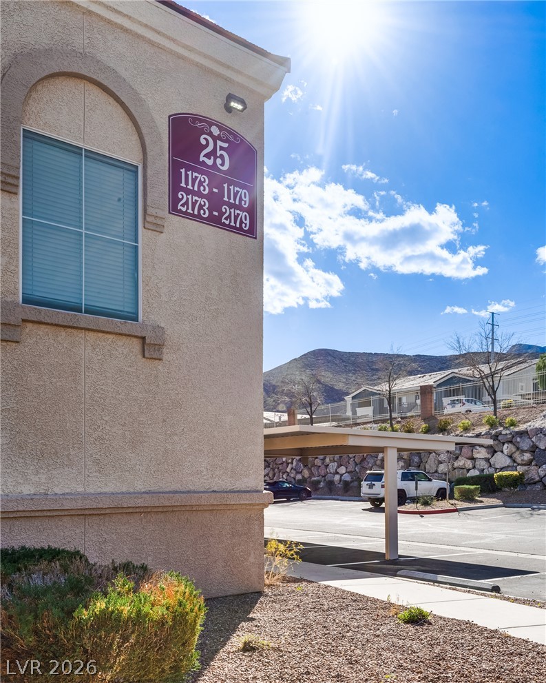 10550 West Alexander Road, Unit 2174 Las Vegas, NV 89129 - Photo 28 of 28 Sunlight bathes the exterior stucco finishes and covered parking spaces against a scenic mountain backdrop.