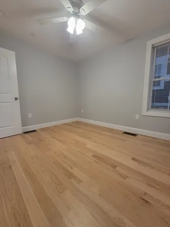 a view of an empty room with wooden floor and a chandelier fan