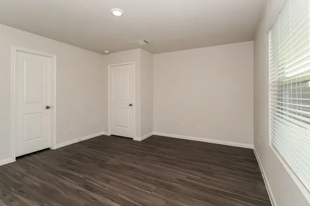 a view of an empty room with wooden floor and a window