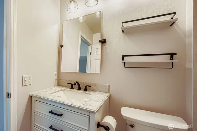 a bathroom with a granite countertop sink vanity mirror and toilet