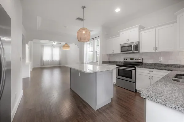 a kitchen with stainless steel appliances granite countertop a refrigerator a stove top oven a sink dishwasher and white cabinets with wooden floor