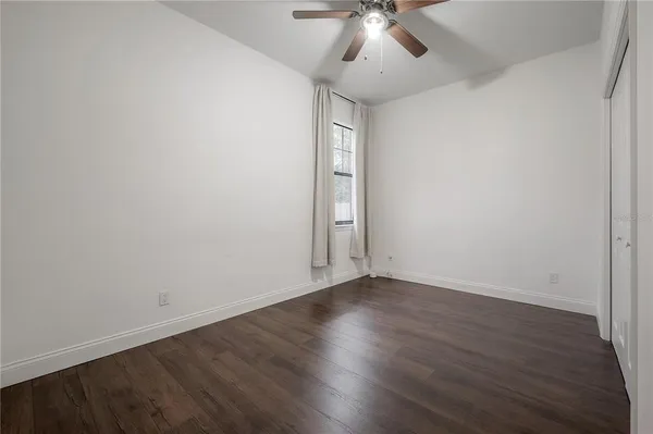 a view of an empty room with wooden floor and a chandelier fan