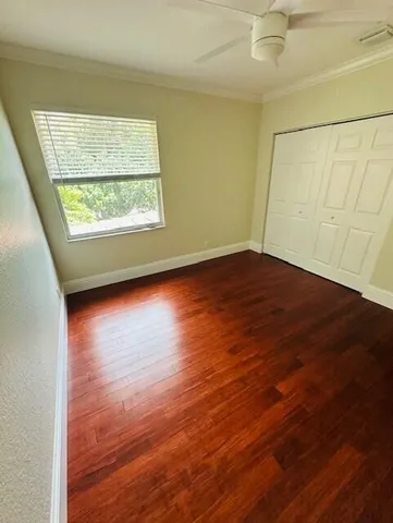 an empty room with wooden floor chandelier fan and windows