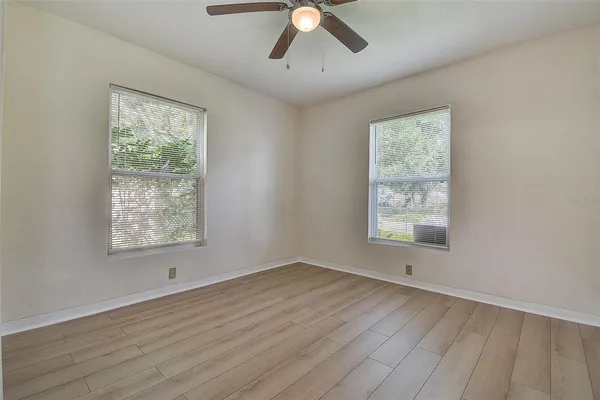 an empty room with wooden floor chandelier fan and windows