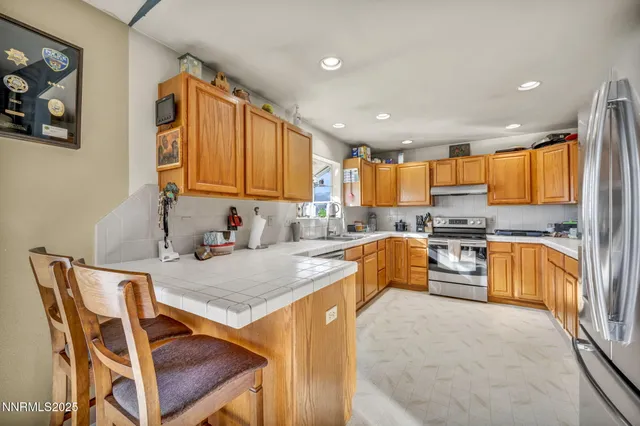 a kitchen with stainless steel appliances granite countertop a stove a sink a microwave a refrigerator white cabinets and couches with wooden floor