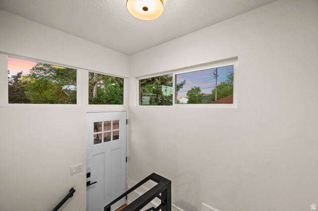 189 West Center Street Midvale, UT 84047 - Photo 26 of 64 White painted door with upper window panes, complemented by multiple high-set horizontal windows, a flush-mount ceiling light fixture, and black metal handrailing to the finished basement