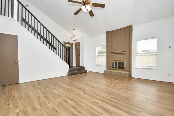 a view of an empty room with wooden floor and a ceiling fan
