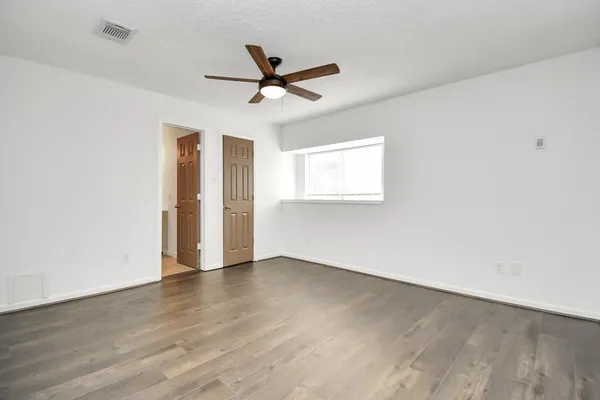an empty room with wooden floor ceiling fan and windows