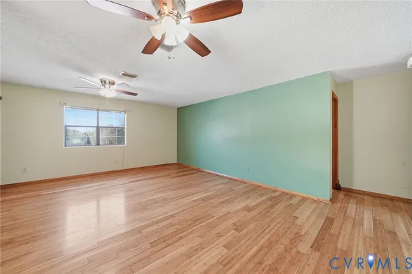 an empty room with wooden floor chandelier fan and windows