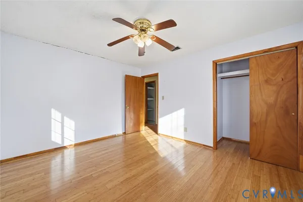 an empty room with wooden floor chandelier fan and windows