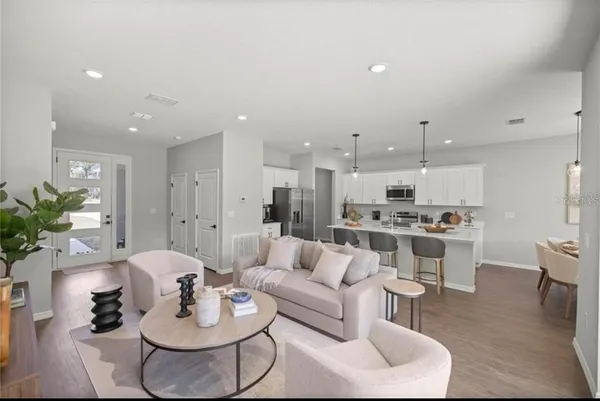 a living room with stainless steel appliances kitchen island granite countertop a sink and white cabinets with wooden floor