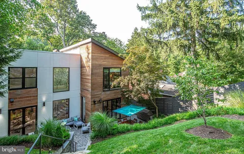a view of a house with brick walls and a yard with plants and large trees