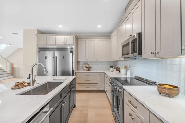 a kitchen with stainless steel appliances kitchen island granite countertop a refrigerator a sink a stove and white cabinets with wooden floor