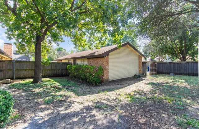 a backyard of a house with large trees and wooden fence