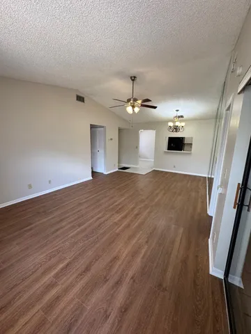 a view of an empty room with wooden floor and a ceiling fan