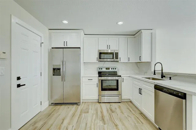 a kitchen with stainless steel appliances granite countertop a refrigerator stove a sink and white cabinets with wooden floor