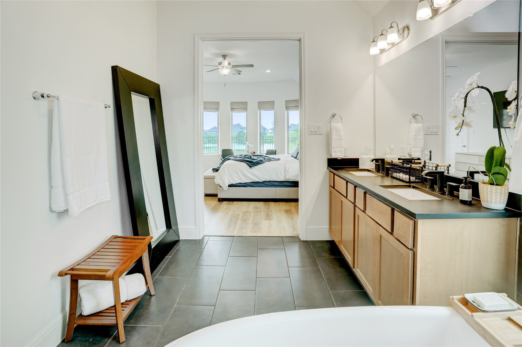 619 Rita Blanca Drive Webster, TX 77598 - Photo 21 of 44 The primary bathroom features sleek, dark tiles and light wood cabinetry, leading into a bedroom with wood inspired floors and large windows offering a scenic view.