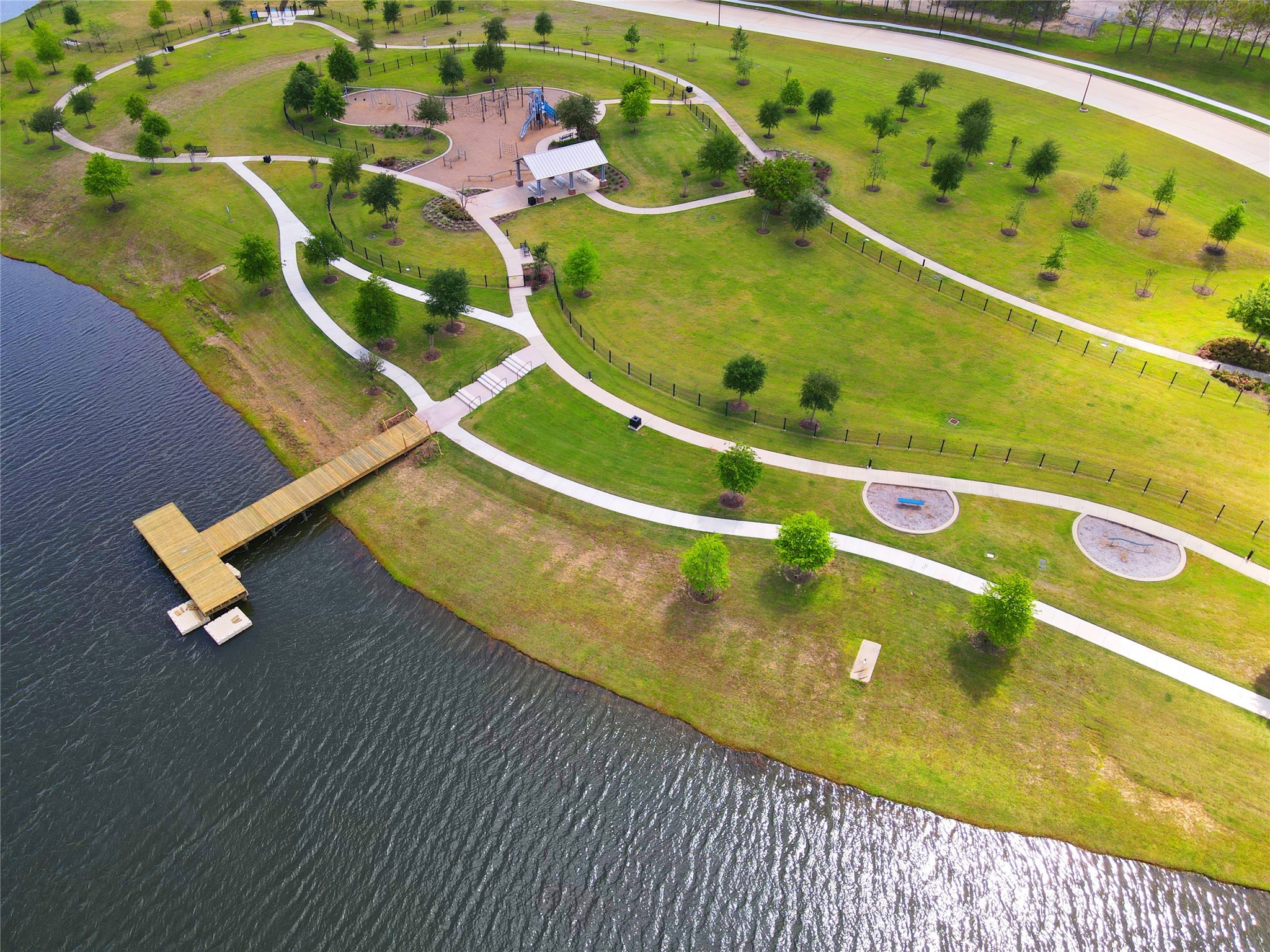 619 Rita Blanca Drive Webster, TX 77598 - Photo 40 of 44 Edgewater's scenic park with lush green spaces, winding pathways, a playground, and a picnic area. It features a waterfront view with a wooden pier extending into the water, ideal for outdoor activities and relaxation.