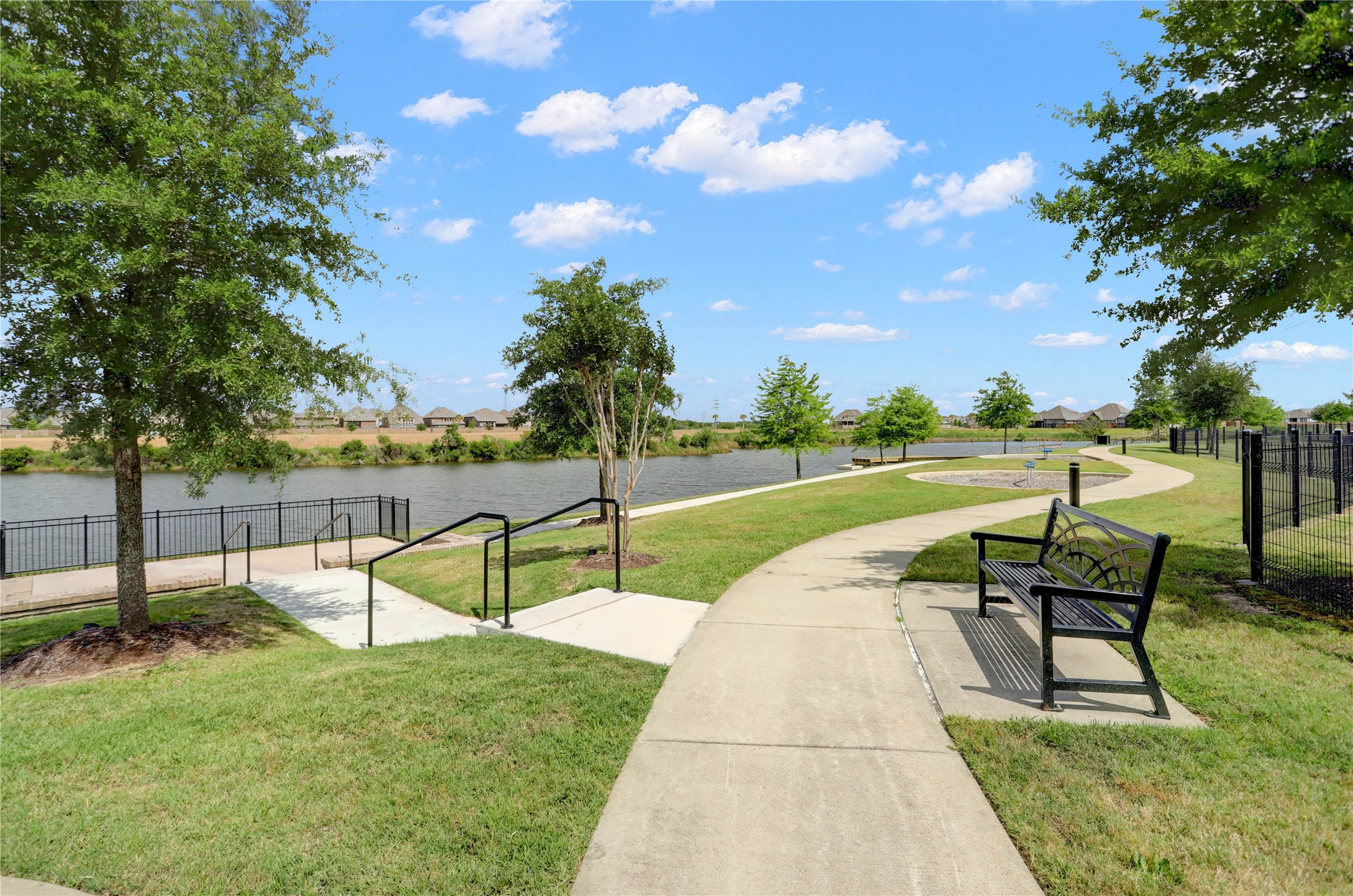 619 Rita Blanca Drive Webster, TX 77598 - Photo 41 of 44 The scenic walking path along the tranquil lake is surrounded by lush greenery and dotted with benches, perfect for relaxation and outdoor enjoyment in a peaceful neighborhood setting.